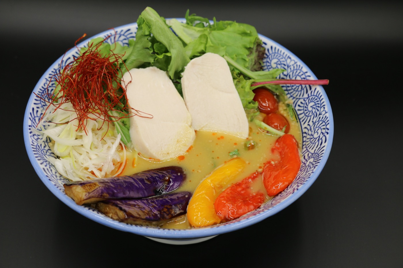Curry ramen with chicken in a blue patterned bowl, topped with colorful vegetables