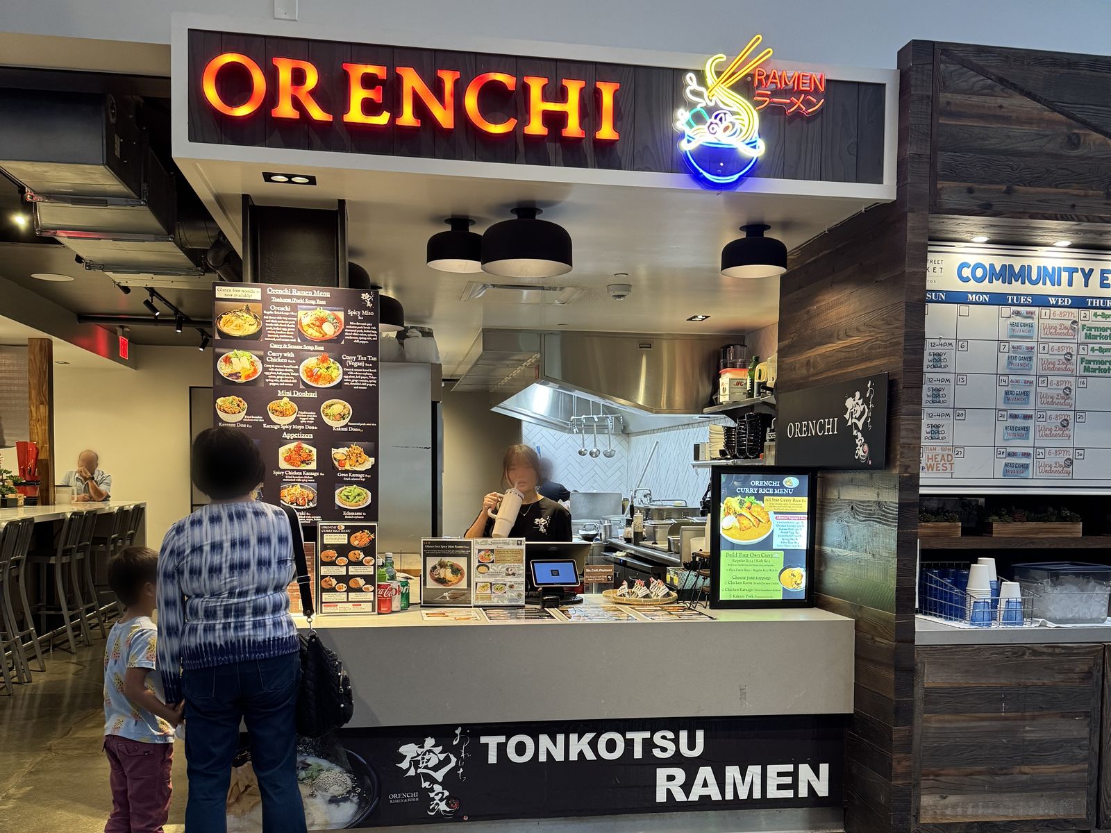 The Orenchi Ramen stall inside State Street Market, with a glowing orange ORENCHI sign, a neon ramen bowl, and a TONKOTSU RAMEN counter front